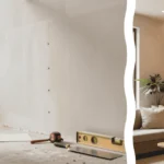 A modern living room featuring a floor to ceiling DIY slatted wood wall budget project with a focused foreground shot of a precision cordless brad nailer resting against a smooth oak slat.