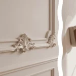 A detailed view of a high-quality adhesive strip being applied to a lightweight trim piece in the foreground with a living room featuring completed removable box molding for rentals on the back wall.